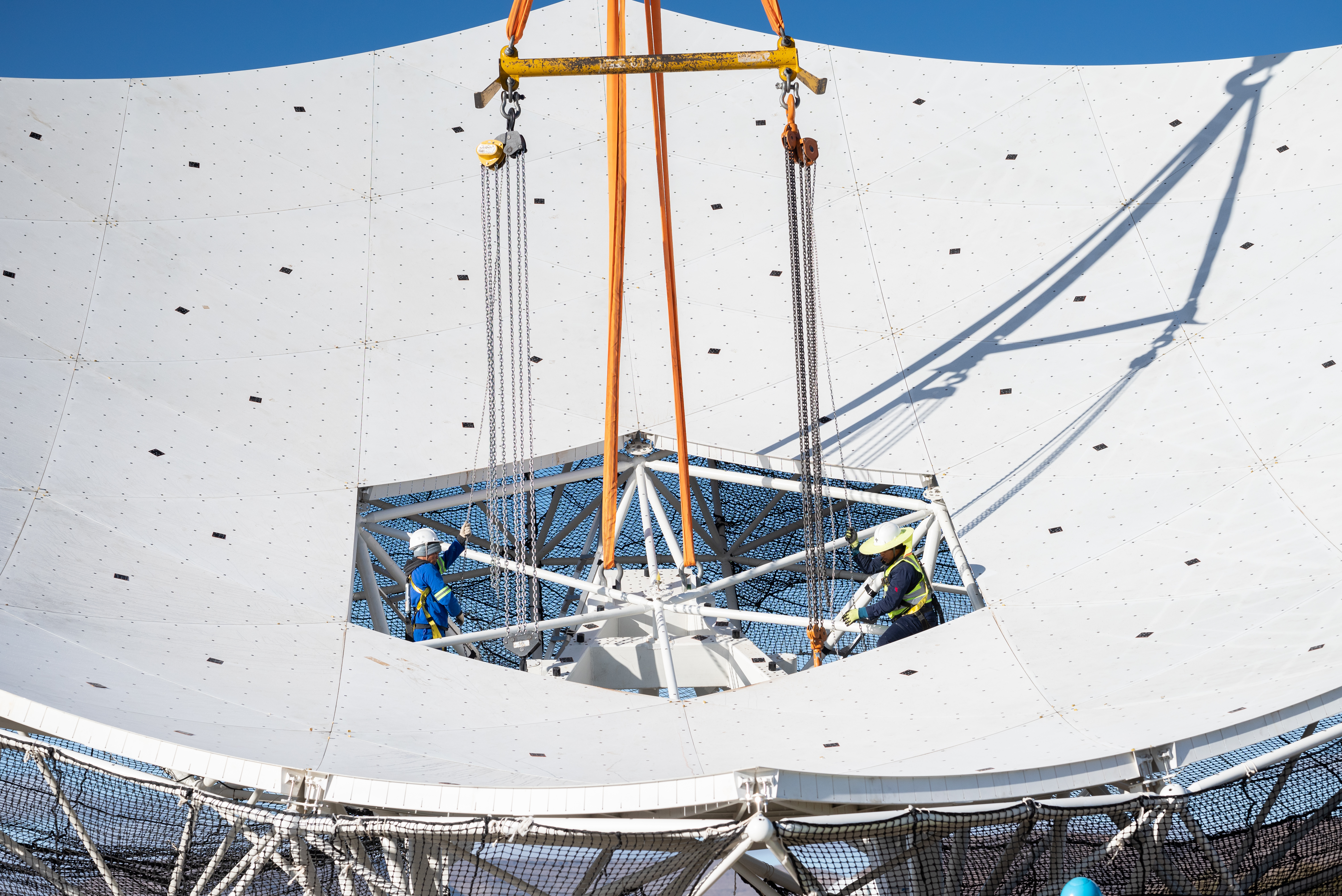 A close up of the reflector being fitted to the pedestal - two team members are within the structure.