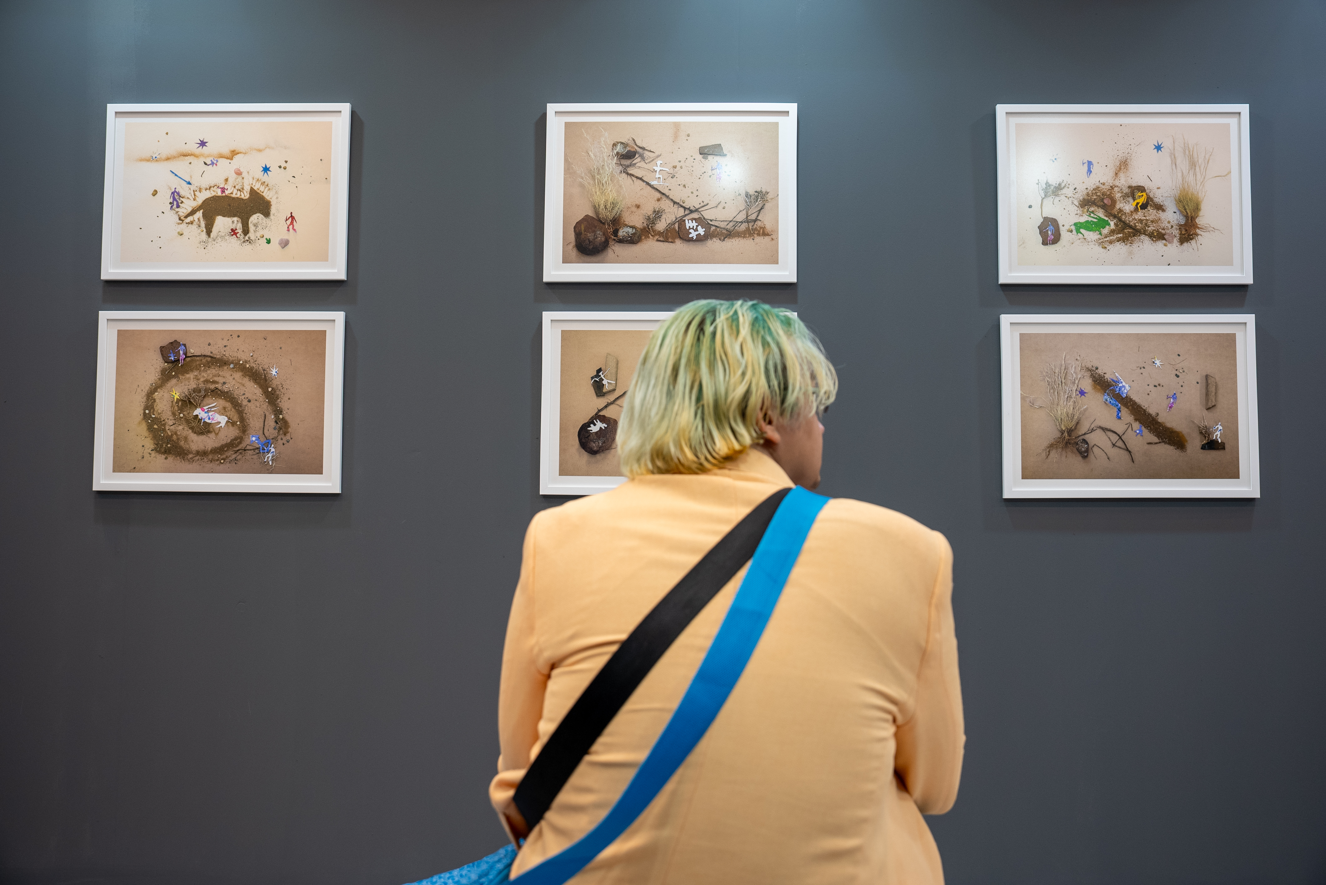 Attendee at the Cosmic Echoes art exhibition in Cape Town sitting in front of artwork created by young people from the Northern Cape, South Africa. Artwork featured: Crossing Oceans Inside, Terence Visagie & Youth Artists 