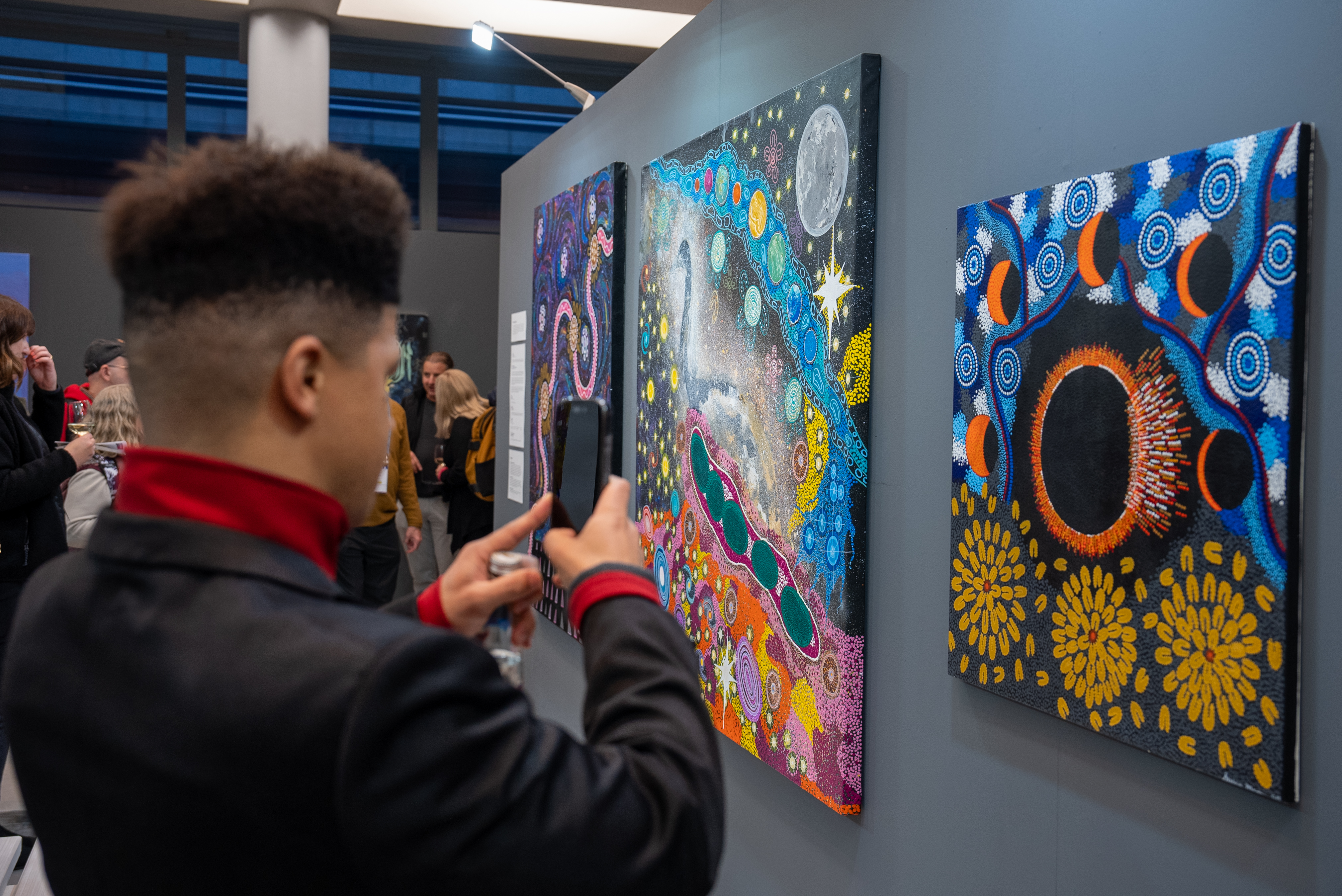 Attendee at Cosmic Echoes launch event in Cape Town taking pictures of the artwork. Artwork featured (L-R) Seven Sisters - Noeleen Hamlett, The First Astronomers - Dawn Hamlett and Leeann Kelly-Pedersen, The Eclipse - Susan Merry