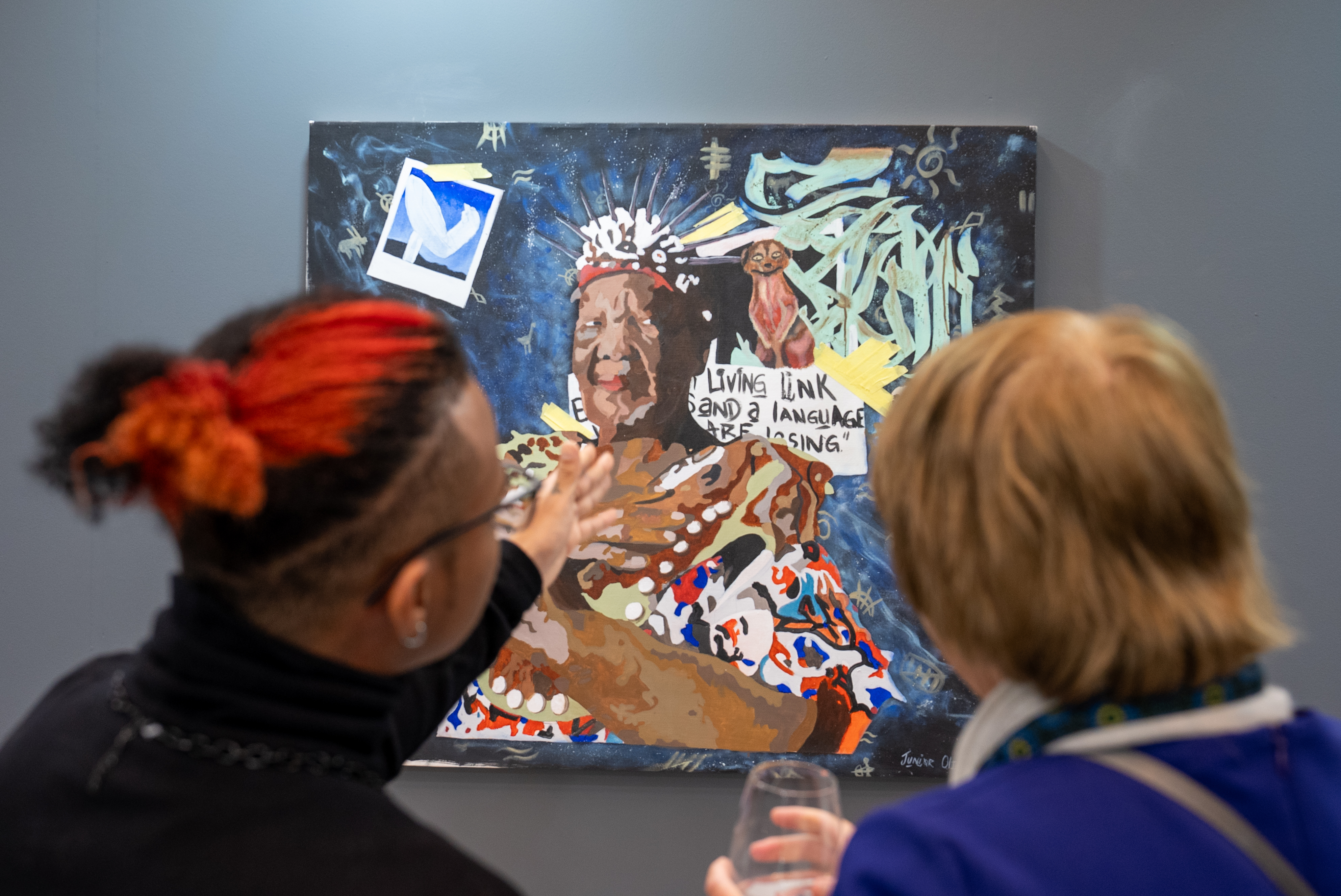 Attendee at the Cosmic Echoes art exhibition in Cape Town speaking to artist, Junior Oliphant. Artwork featured: Children of the San XI: My Ma Se Taal, Junior Oliphant 