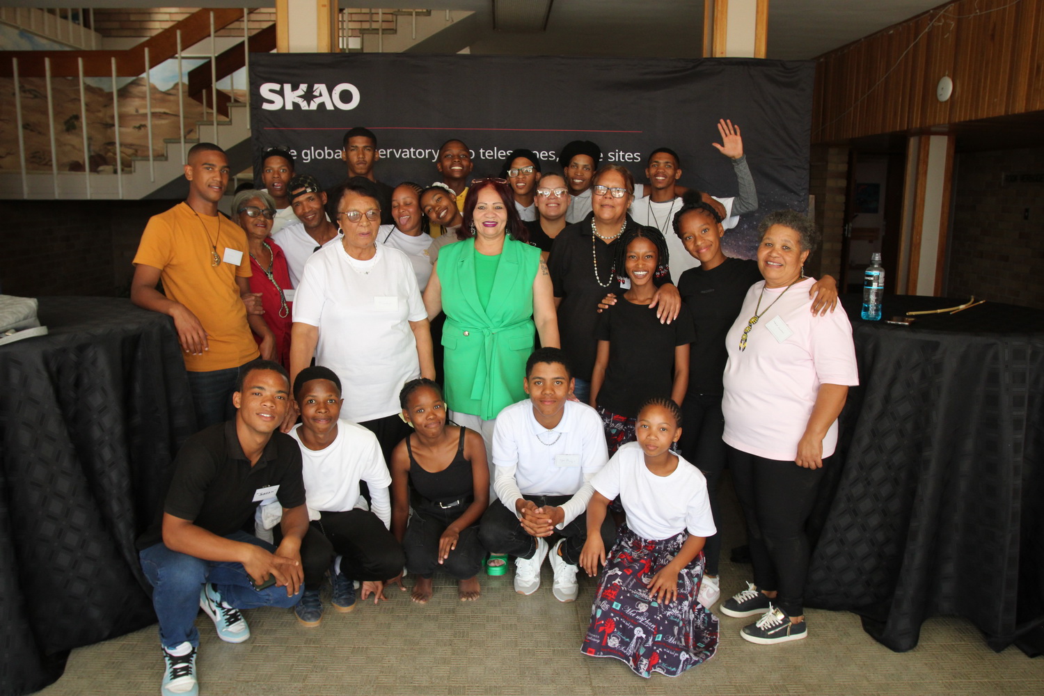 A group photos of the Carnarvon youth artists with Elders from the community. Behind them is an SKAO banner.