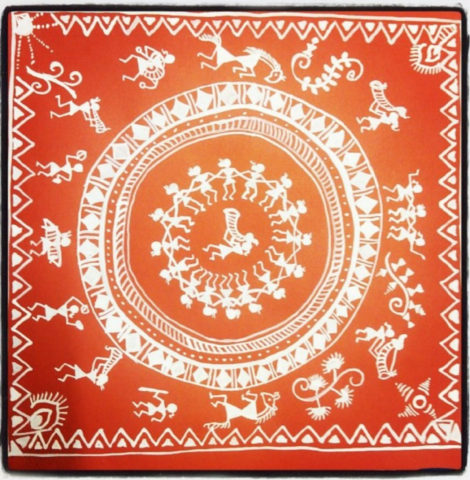 A Warli painting created by Snehal Valame, a type of Indian tribal art. It is orange/red with white figures painted on to it in a circular pattern