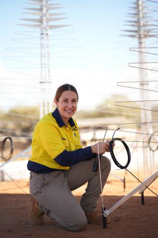 Angela Teale wearing a hi-vis shirt and working on an antenna on site in Australia. She is holding a cable and a screwdriver.
