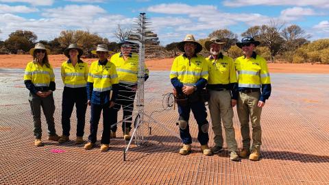 Seven team members in hi-vis safety jackets standing with the first SKA-Low antenna installed on site