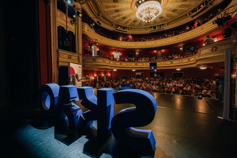 A view from the stage of the SKAO science meeting showing the SKAO logo in large cut out letters on the stage, and a packed theatre in the background.