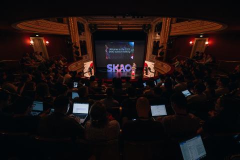 A view from the top of the auditorium during the SKAO science meeting, with people on laptops, and the stage in the background with the SKAO logo