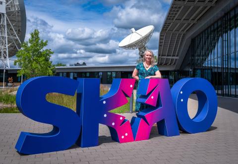 Picture of Prof. Jessica Dempsey standing behind big letters that read "SKAO" in front of the SKAO Global Headquartes.