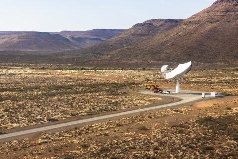Aerial view of one SKA-Mid dish with a road leading to it against a mountainous landscape.