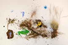 Composition of different elements: figures of animals and people sitting on a tree made from natural elements such as twigs, rocks and grass, with some stars above them. 