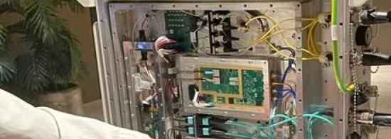 A picture of someone pointing at an SKA-Mid digitiser. The digitiser looks like an opened-up desktop computer with various components, circuits and cables. 
