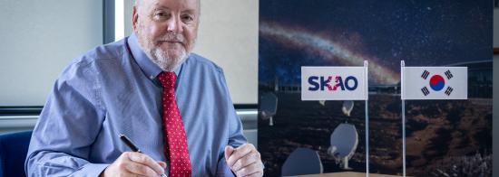 SKAO Director-General Prof. Philip Diamond signing a document. Next to him are small SKAO and Korean flags on the desk.