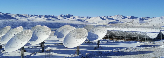 Nine telescope dishes and three open cylindrical telescopes in a snowy mountainous landscape under clear blue skies. 