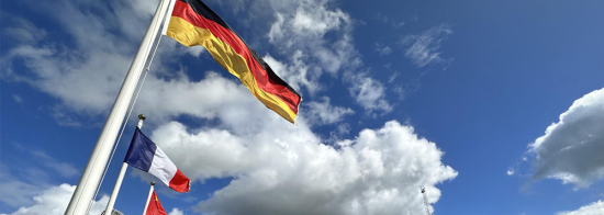 German flag waving against a blue sky with clouds. 