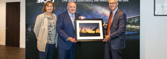 Photo of three people, from left: STFC Executive Chair Michele Dougherty, SKAO Director-General Prof. Philip Diamond, and UK Minister of State for Science, Research and Innovation Lord Patrick Vallance. Prof. Diamond is handing Lord Vallance a frame photograph of the SKA telescopes. In the background is an SKAO banner.