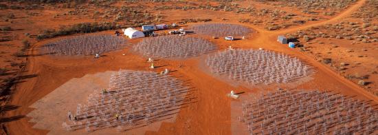 Aerial view of a cluster of 7 SKA-Low antenna stations. Six stations are completely and the seventh half filled with telescope antennas that look like metal Christmas trees.