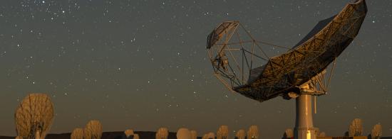Nighttime view of an SKA-Mid dish with the MeerKAT radio telescope in the background. The sky is full of stars.