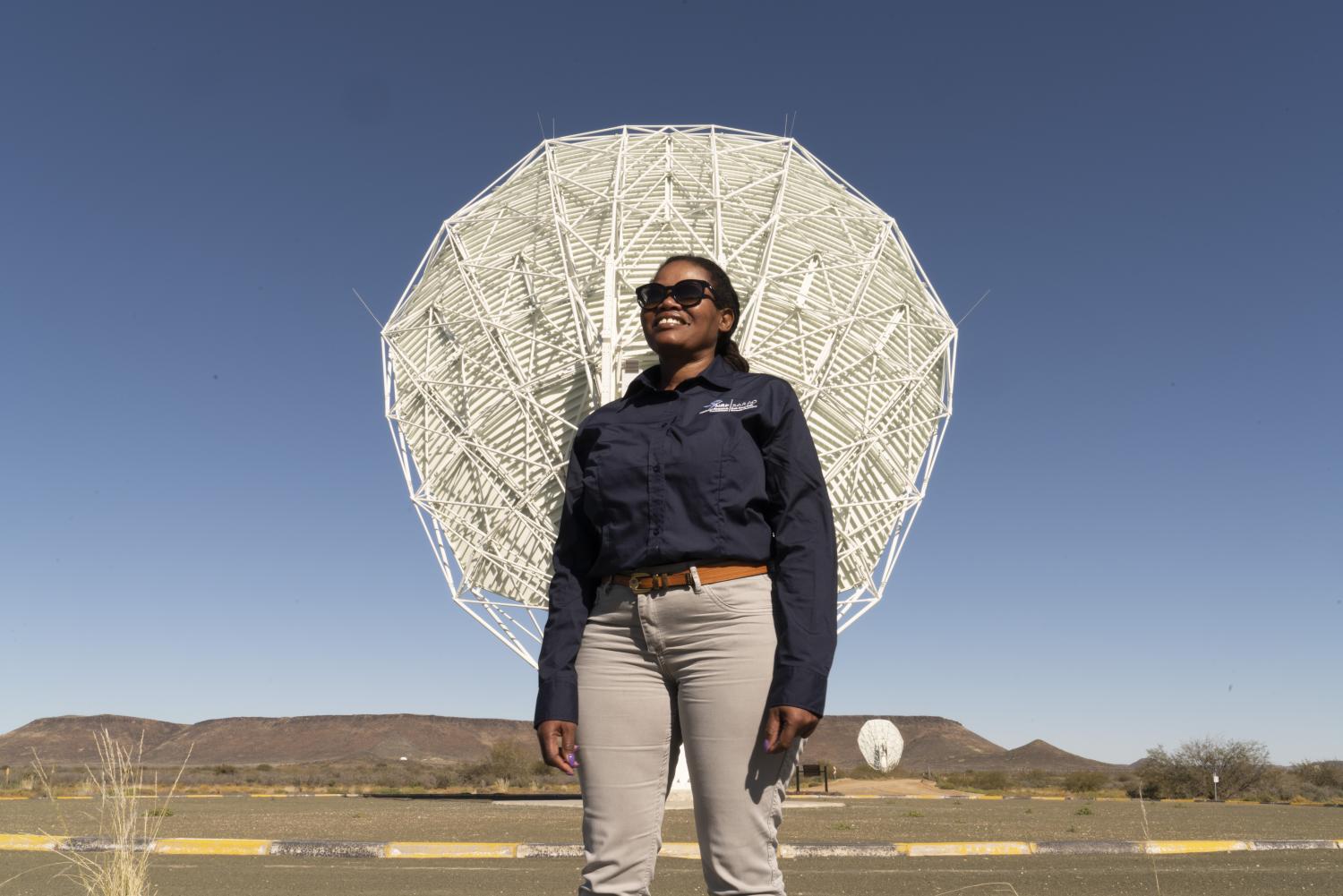 Picture of Pontsho Maruping standing proudly in front of a telescope dish.