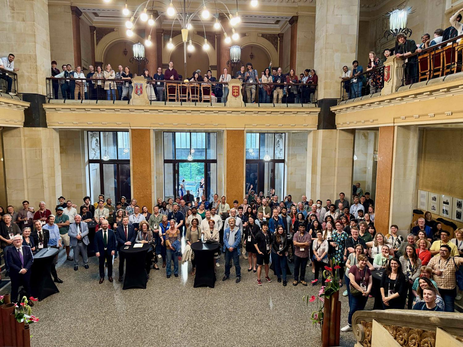 Group photo hundreds of attendees at the SKAO science meeting, in a grand entrance foyer. Some are on the ground floor, while others are standing on a mezzanine level.