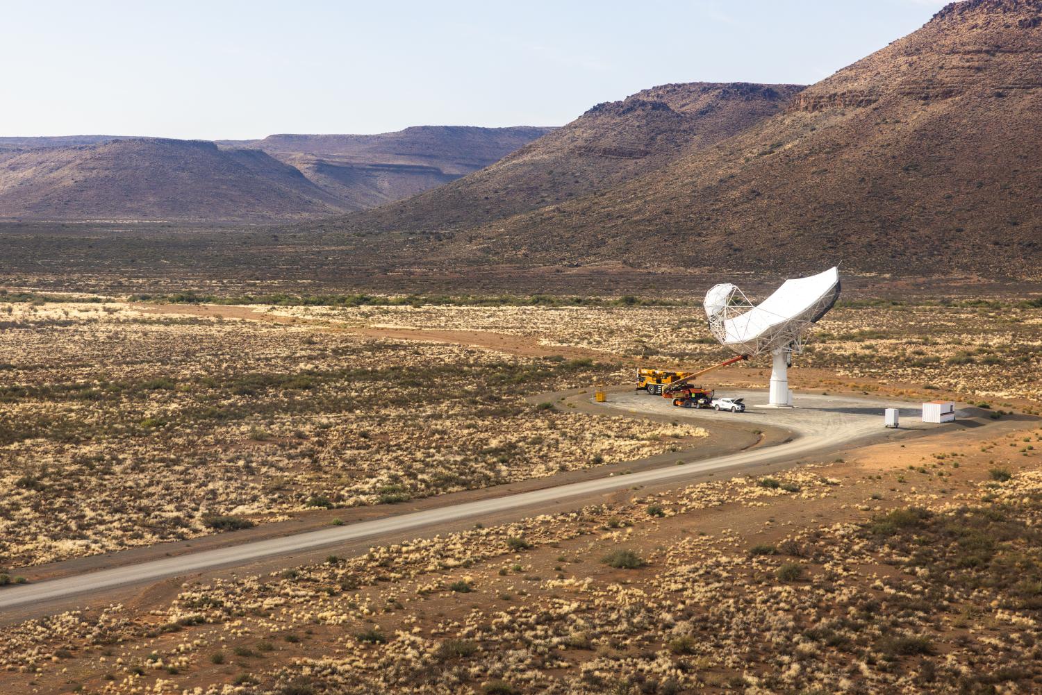 Aerial view of one SKA-Mid dish with a road leading to it against a mountainous landscape.