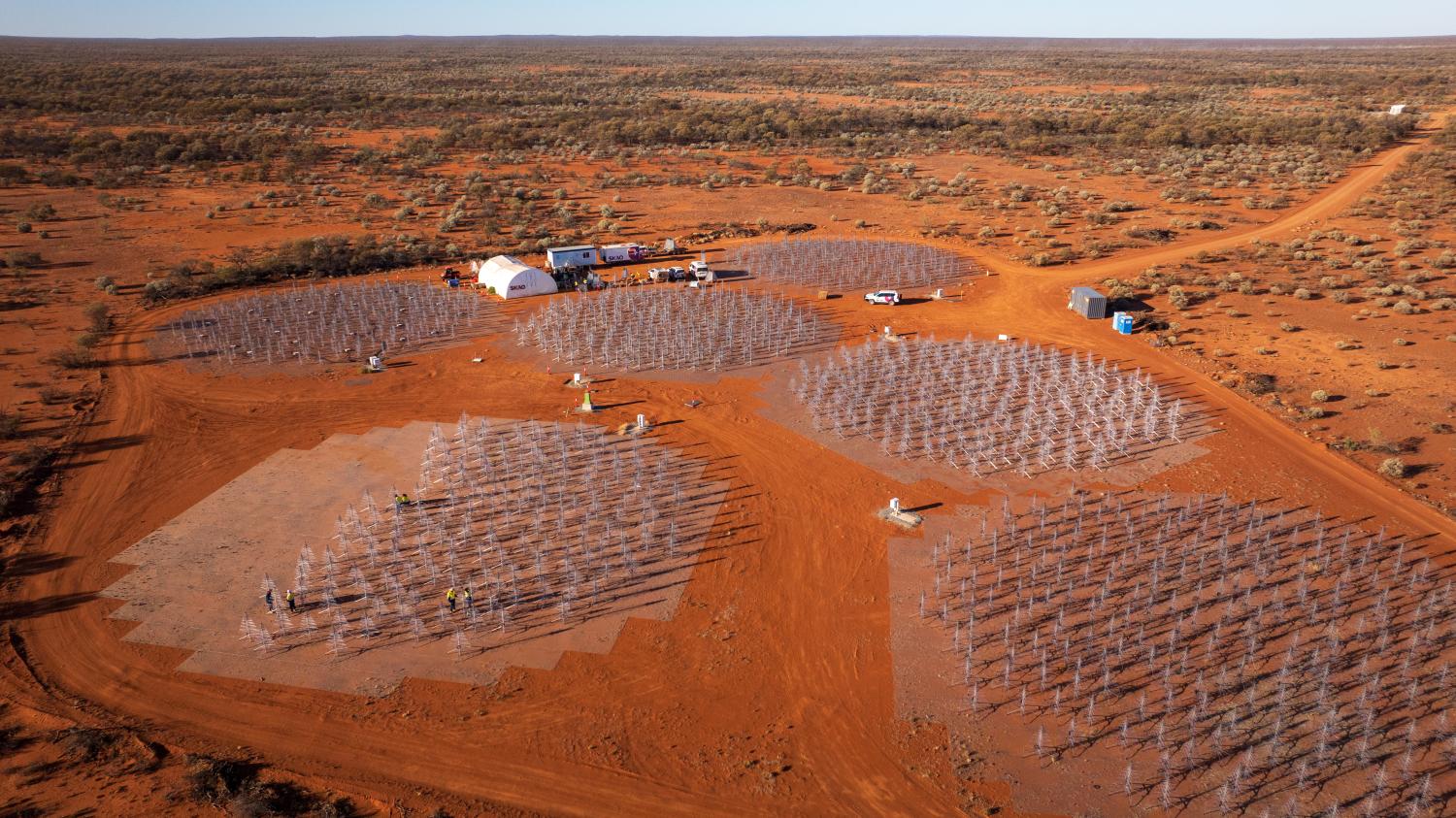 Aerial view of a cluster of 7 SKA-Low antenna stations. Six stations are completely and the seventh half filled with telescope antennas that look like metal Christmas trees.