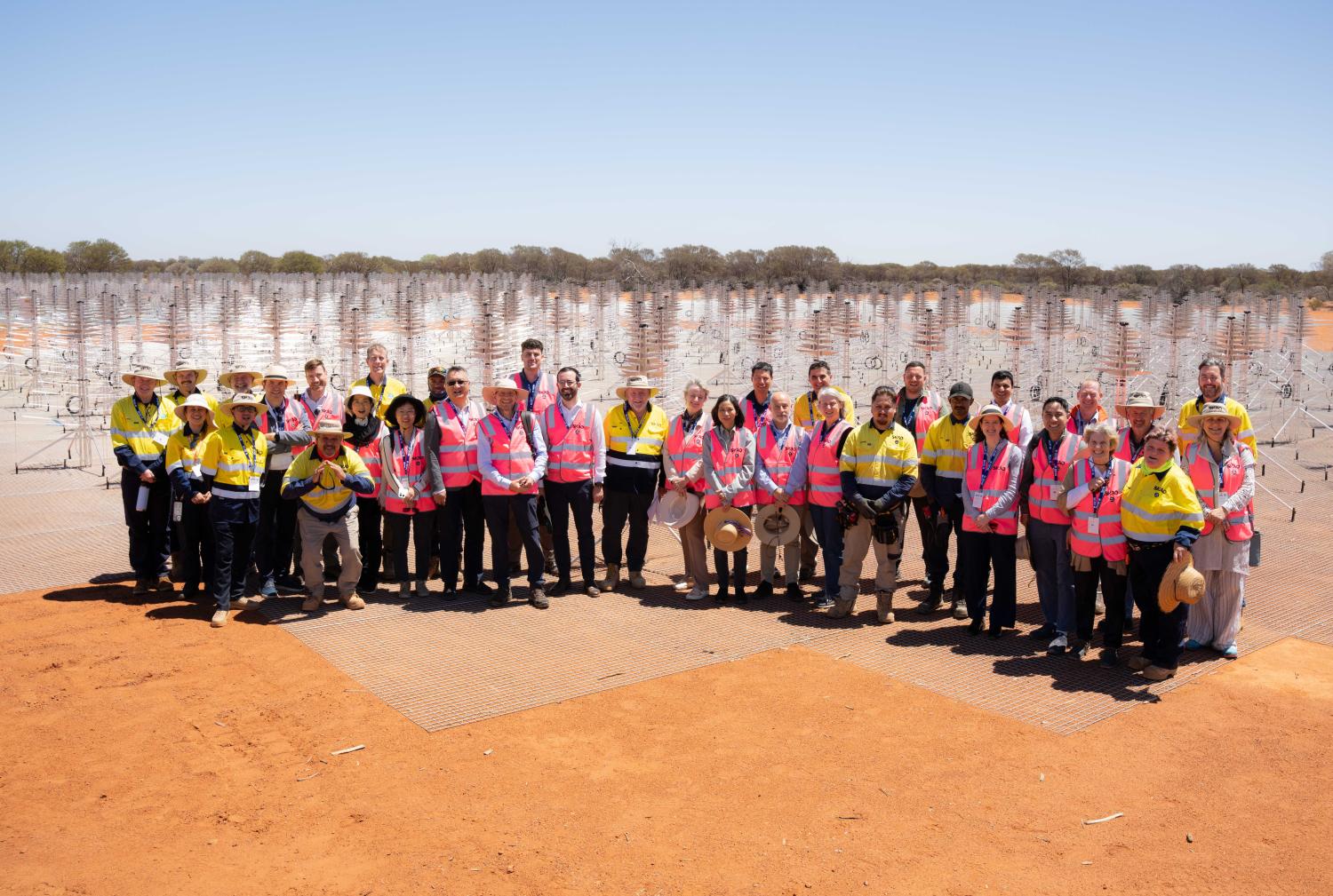 Group photo of around 35 people in hi-vis jackets standing in front of an SKA-Low station