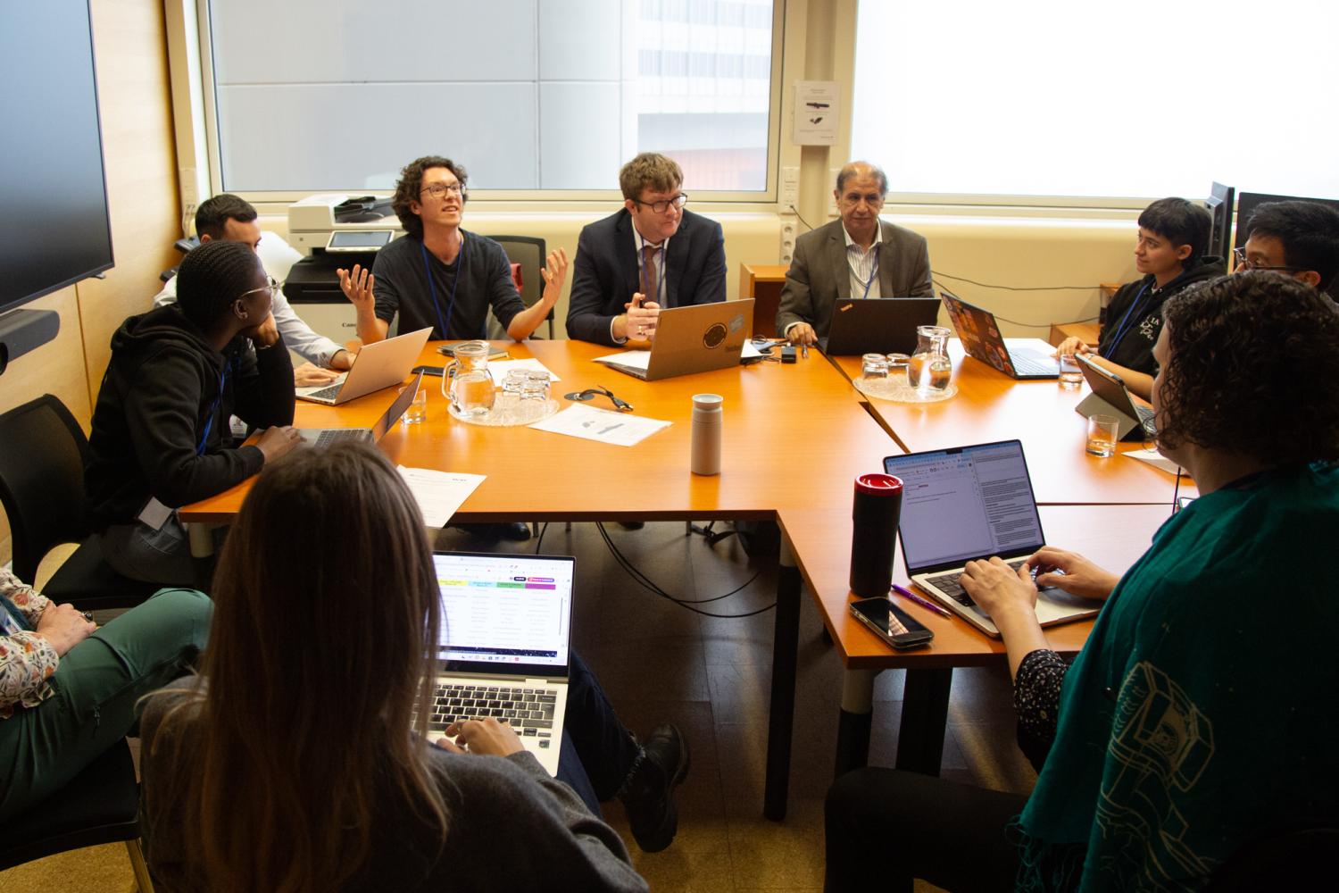 People sitting in a circle around a table working on their laptops and discussing.