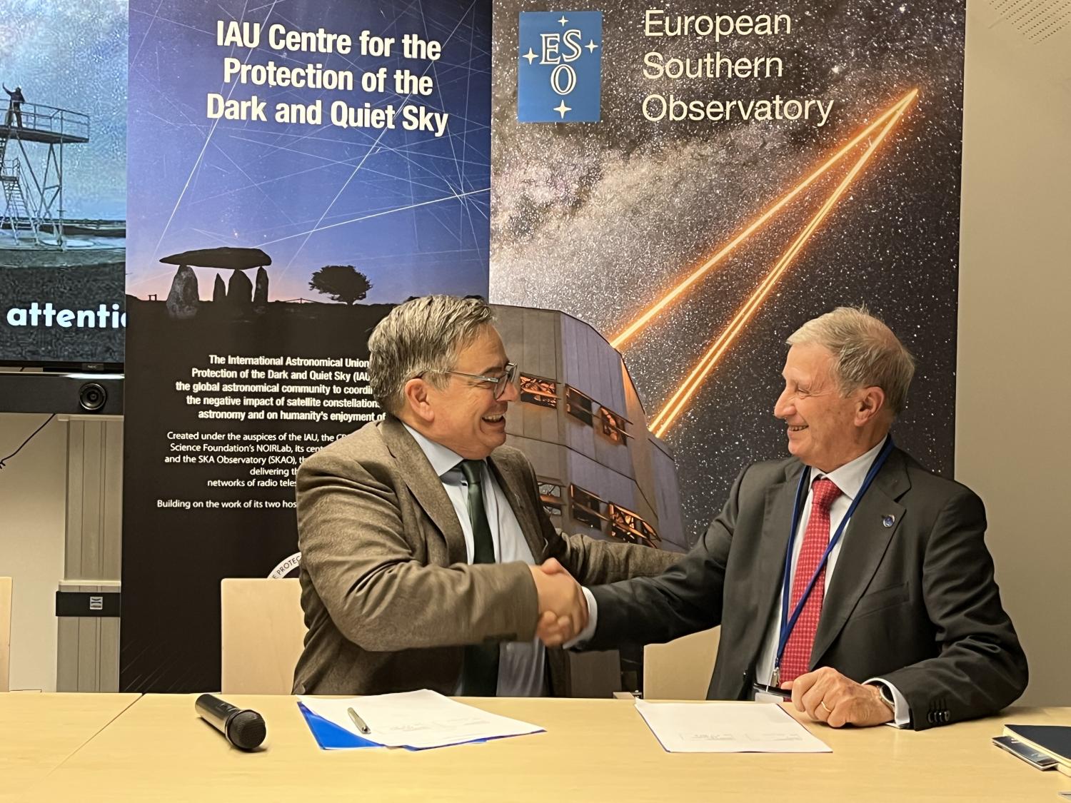 Two men shaking hands in the front of an IAU CPS and ESO banner.