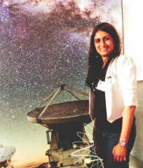 Snehal Valame standing in front of large image of a telescope and the night sky